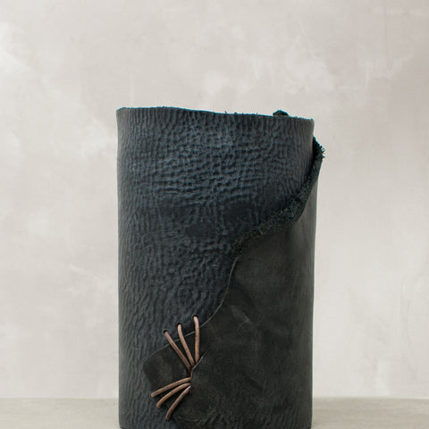 Image of navy leather wrapped vase stitched with charcoal leather cord on a stone table.