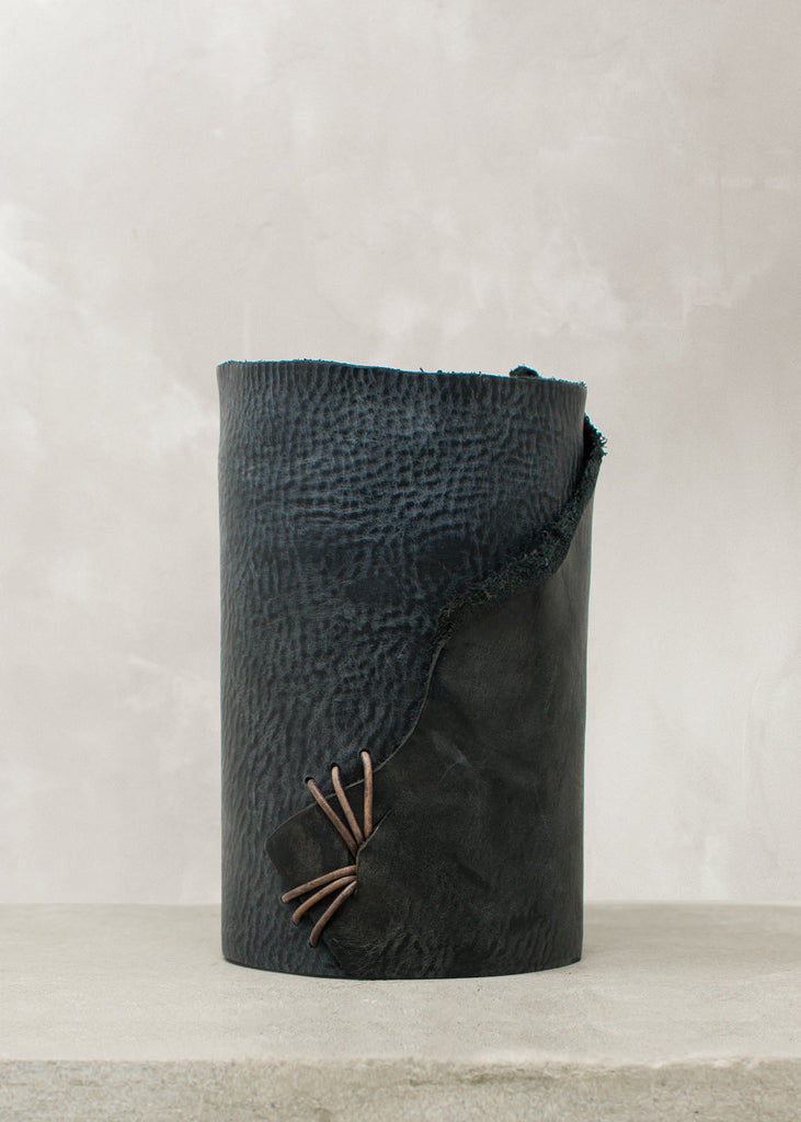 Image of navy leather wrapped vase stitched with charcoal leather cord on a stone table.